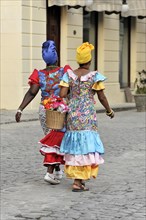 Two Creole women in colourful costumes walking in the centre of Havana, Cuba, Greater Antilles,