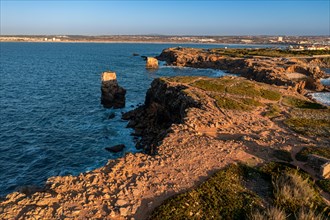 Bird's-eye view of ocean waves break on rocky shores pf Peniche, Portugal. Summer sunset haze,