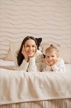 Beautiful young mother and her little daughter lying on bed together