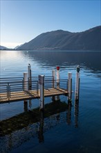 Jetty on Lake Lugano with Mountain and Sunlight Against Blue Clear Sky in Campione d'Italia,
