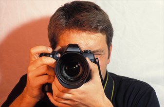 Young man, Photographer with camera taking a picture, focusing, portrait, camera in front of the