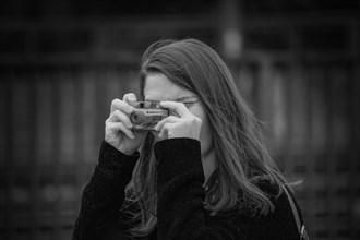 Young woman holds a camera in front of her face and concentrates on taking pictures, Hohenzollern
