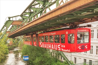 Red suspension railway with advertising runs over an urban river landscape, suspension railway,