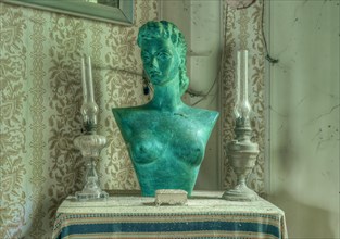 A green bust between two candlesticks on a table in front of a window, Maison Limmi, Lost Place,