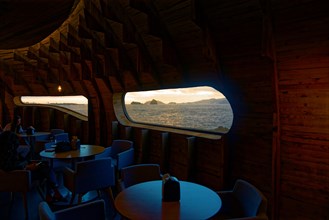 Cosy wooden interior of the Cella Bar with large windows overlooking the ocean at sunset, Madalena,