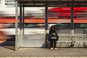 Young woman sitting on the platform looking at her mobile phone while a train passes by, Giessen