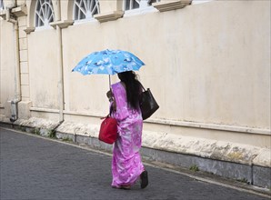 Woman walking with umbrella for shade by the fort walls in the historic town of Galle, Sri Lanka,