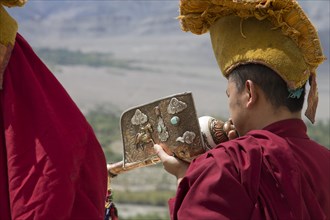 A Buddhist monk playing a dung dkar, the Tibetan conch shell drum, standing on the roof of Thikse