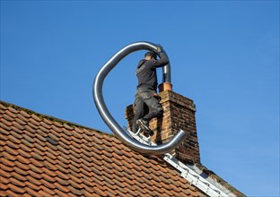 Man fitting chimney liner on roof of home, Shottisham, Suffolk, England, UK