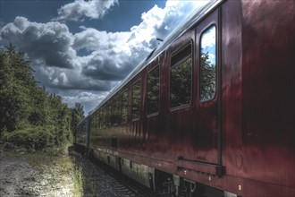 Red railway wagon on tracks under cloudy sky next to green bushes, Dornap-Hahnenfurth railway