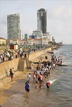School children paddle in the sea on small sandy beach at Galle Face Green, Colombo, Sri Lanka,
