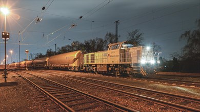 At night at the station, a grey diesel locomotive stands on the tracks next to freight wagons, Ruhr