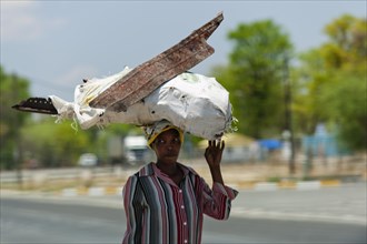 African woman carrying scrap metal on her head through the streets, street scene, Kongola in