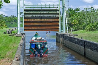 Small traditional wooden fishing boat leaving lock, sluice gate on the Saramacca River at the