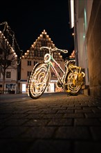 Luminous bicycle with fairy lights in front of a half-timbered house at night, Nagold, Black