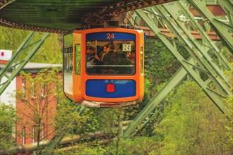 Orange-coloured suspension railway hanging on rails over a green landscape, suspension railway,