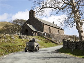 Farmer driving quad bike past village church, Buttermere, Cumbria, England, UK