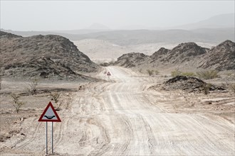 A warning sign stands in front of a sandy desert road, Safari, GravelRoad, unpaved roads, gravel