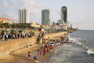 School children paddle in the sea on small sandy beach at Galle Face Green, Colombo, Sri Lanka,