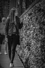 Woman walking along a bridge with many padlocks, black and white photograph, Hohenzollern Bridge,