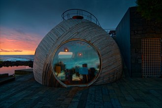Spherical wooden building of the Cella Bar with modern design at sunset, reflections on the glass