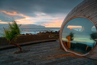 Round window of the wooden extension of the famous Calla Bar and view of the coast at sunset,