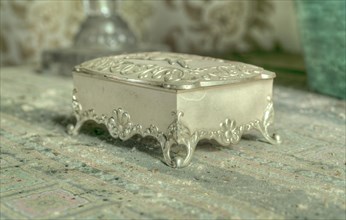 A small, decorated silver jewellery box on a surface with a vintage look, Maison Limmi, Lost Place,