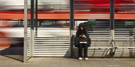Young woman sitting on the platform looking at her mobile phone while a train passes by, Giessen