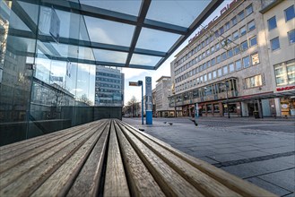 View along a wooden bench onto a square with glass walls and buildings, Leopoldplatz, Pforzheim,