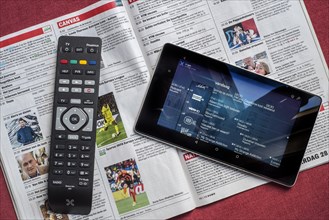 Remote control and tablet showing television channels on top of open Belgian magazine showing the