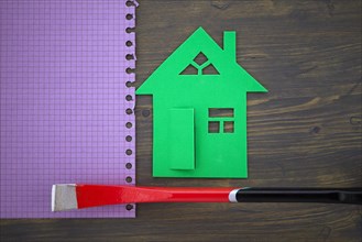 Green cutout of model house with hand tool on a memo notepad in a concept of home ownership,