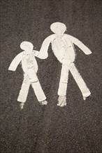 Child and parent figures holding hands on tarmac pavement, Mumbles, South Wales, UK