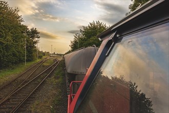 View from the rear-view mirror of a locomotive onto a goods train and tracks in the evening light,
