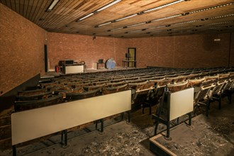 An abandoned lecture theatre with damaged wooden seats and a spherical model on the stage, Biotech,