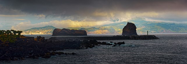 Dark clouds over a calm sea with the island of Faial in the distance and the rock formations Ilheu