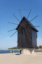Close-up of a historic windmill on the dam in front of a bright blue sky by the sea, landmark,