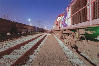 Red locomotive and wagons standing on tracks at night under artificial light, Ruhr area, North