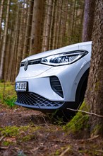 White Deer Carsharing electric car from Volkswagen partially covered by a tree in the forest,