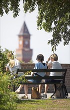 Swedish woman sitting on a park bench, behind them the tower of the town hall, Helsingborg, Skane