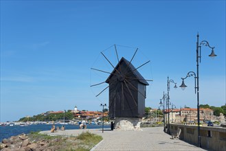 Traditional windmill on the embankment on a sunny day on the coastal promenade with blue sky,