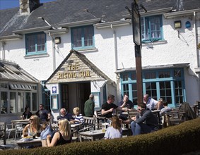 People sitting outside The Rising Sun pub, St Mawes, Cornwall, England, UK