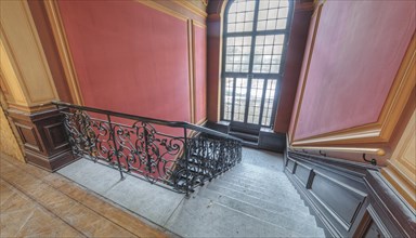Entrance area with curved staircase, red walls and wooden elements, Villa Woodstock, Lost Place,
