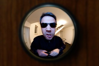 View through door viewer into a staircase, peephole, spyhole, with a man in front of the door,