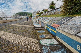 Colourful wall art of Atlantic crossings along a harbour wall with walkers and sailing boats in the