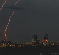 Lightning strikes at night in an urban industrial landscape, illuminated by various lights,