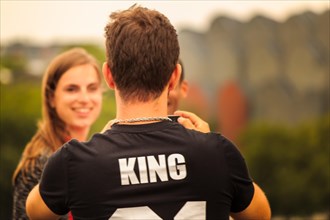 Back view of a couple, with a man wearing a T-shirt with the inscription 'KING',