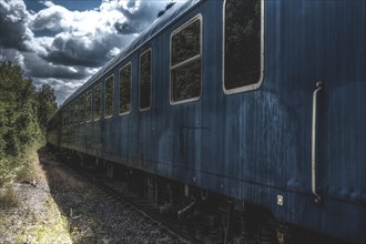 Blue carriage of a train on abandoned tracks surrounded by nature and dramatic clouds,