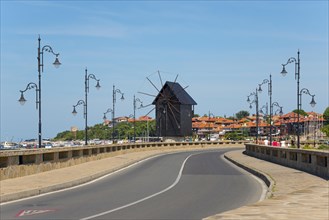 A tidy coastal road leads to a traditional windmill under a bright blue sky, Historic windmill on