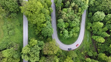A red and a black car driving on a serpentine road through a green landscape, drone shot, Upper