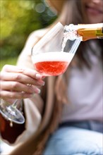 Vertical image of unrecognizable woman holding a glass cup while being served some red champagne